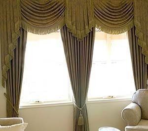 An elegant window with gold draped curtains and valances besides armchairs in a bright living room