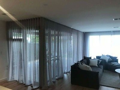 A living room with sheer grey curtains, a dark sofa, and bright natural light from large windows