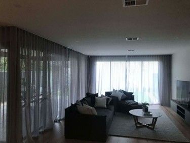 A living room with sheer grey curtains, dark sofas, a round coffee table, and a TV unit