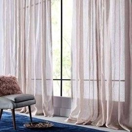 Light pink sheer curtains hanging on tall windows with a blue rug and modern chair in front