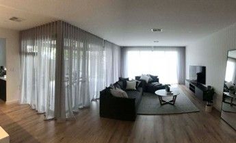 A living room with sheer grey curtains, dark sofas, a round coffee table, a TV unit, and a mirror