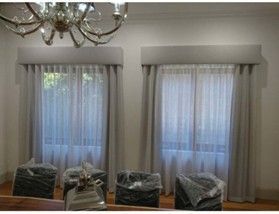 Two windows with sheer white curtains and grey drapes under pelmets in a dining room