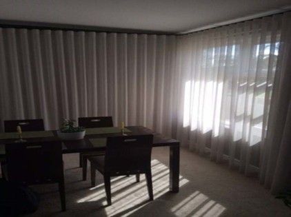 A dining room with a dark wooden table and chairs near large windows covered by sheer white curtains