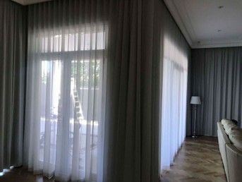 A modern living room with sheer white curtains over large windows and a floor lamp near a sofa