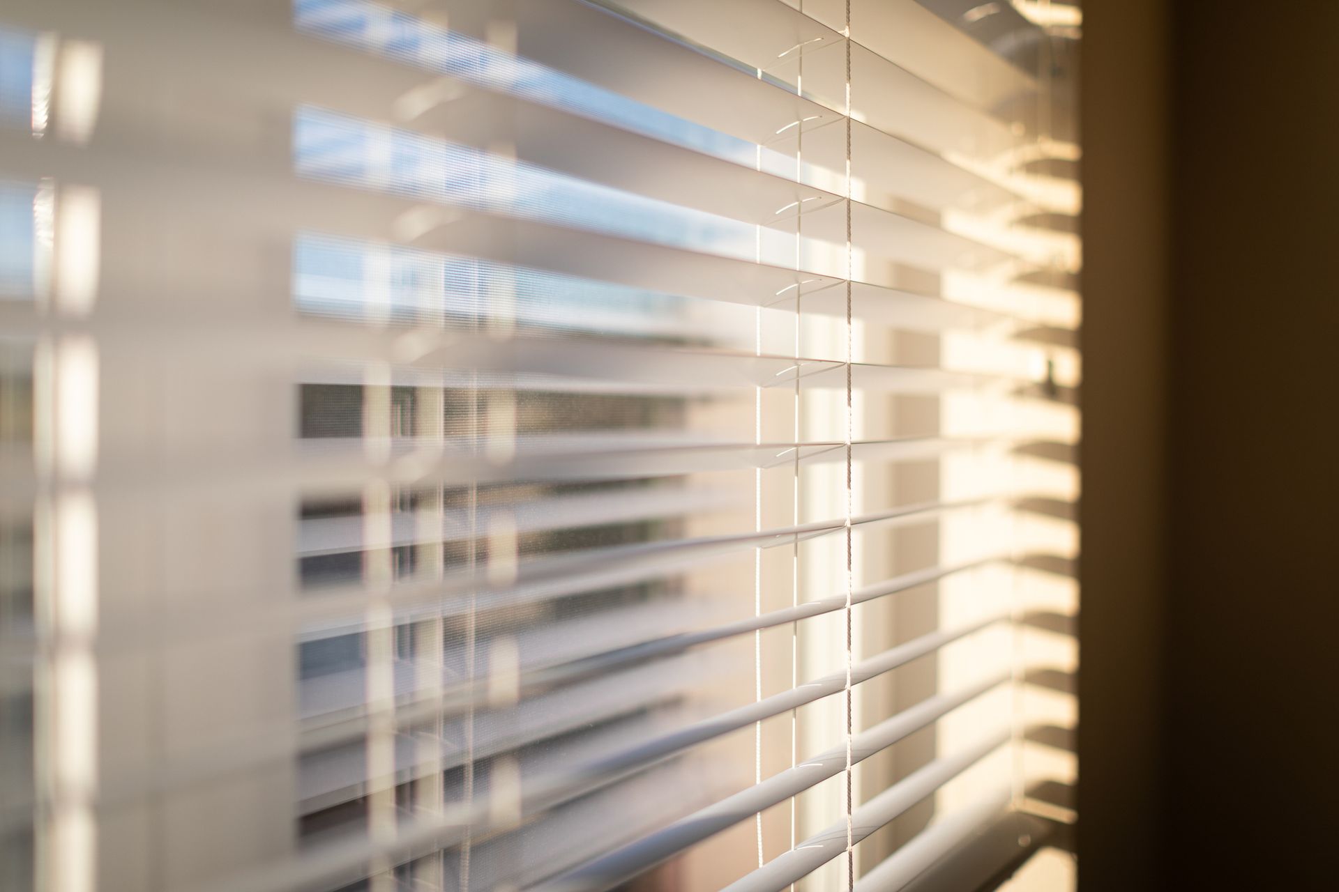 Window view with sunlight shining through venetian blinds, brightening the interior living space.