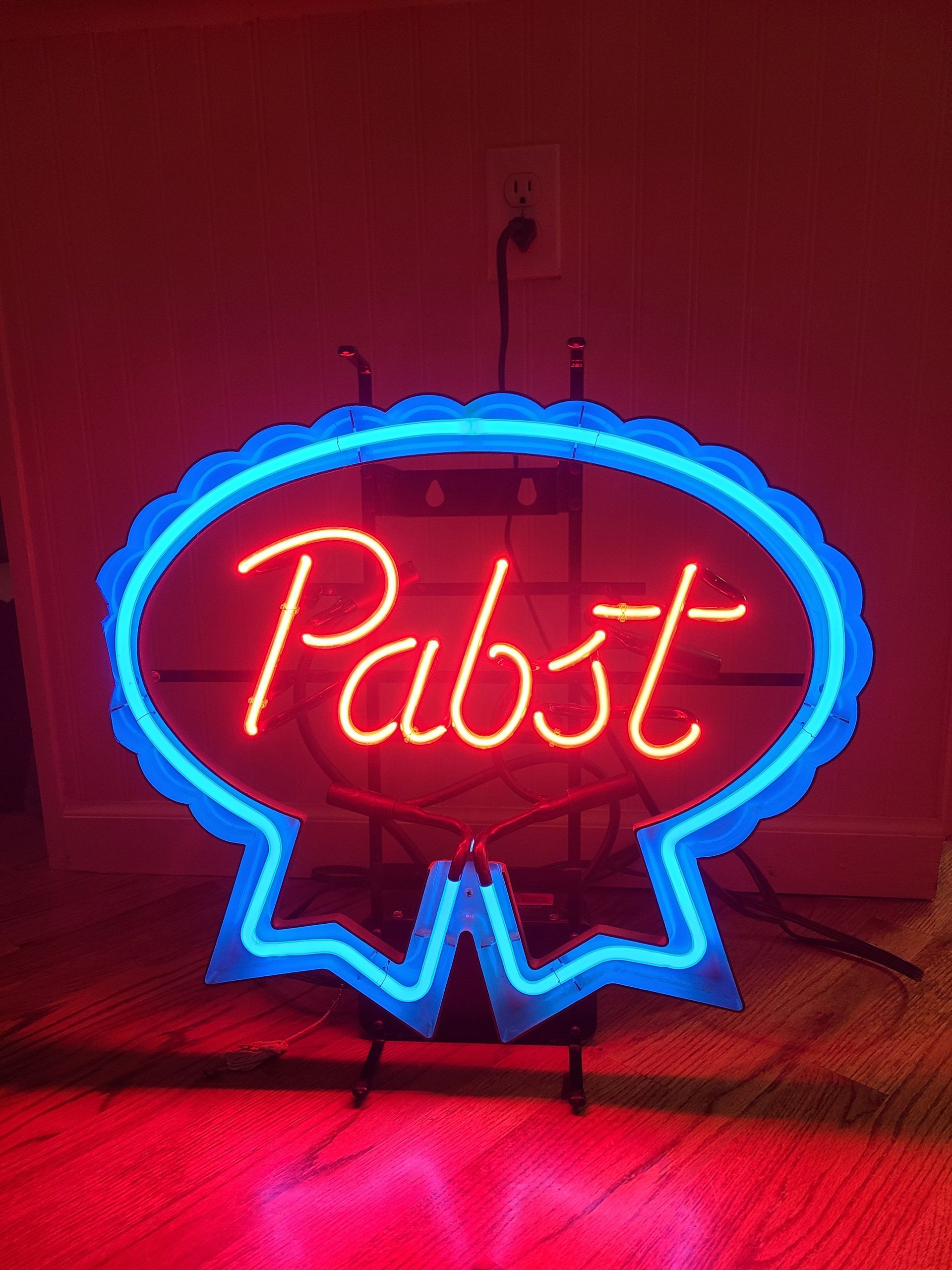 Neon Pabst Blue Ribbon beer sign. Red and blue glow on a stand in a room.