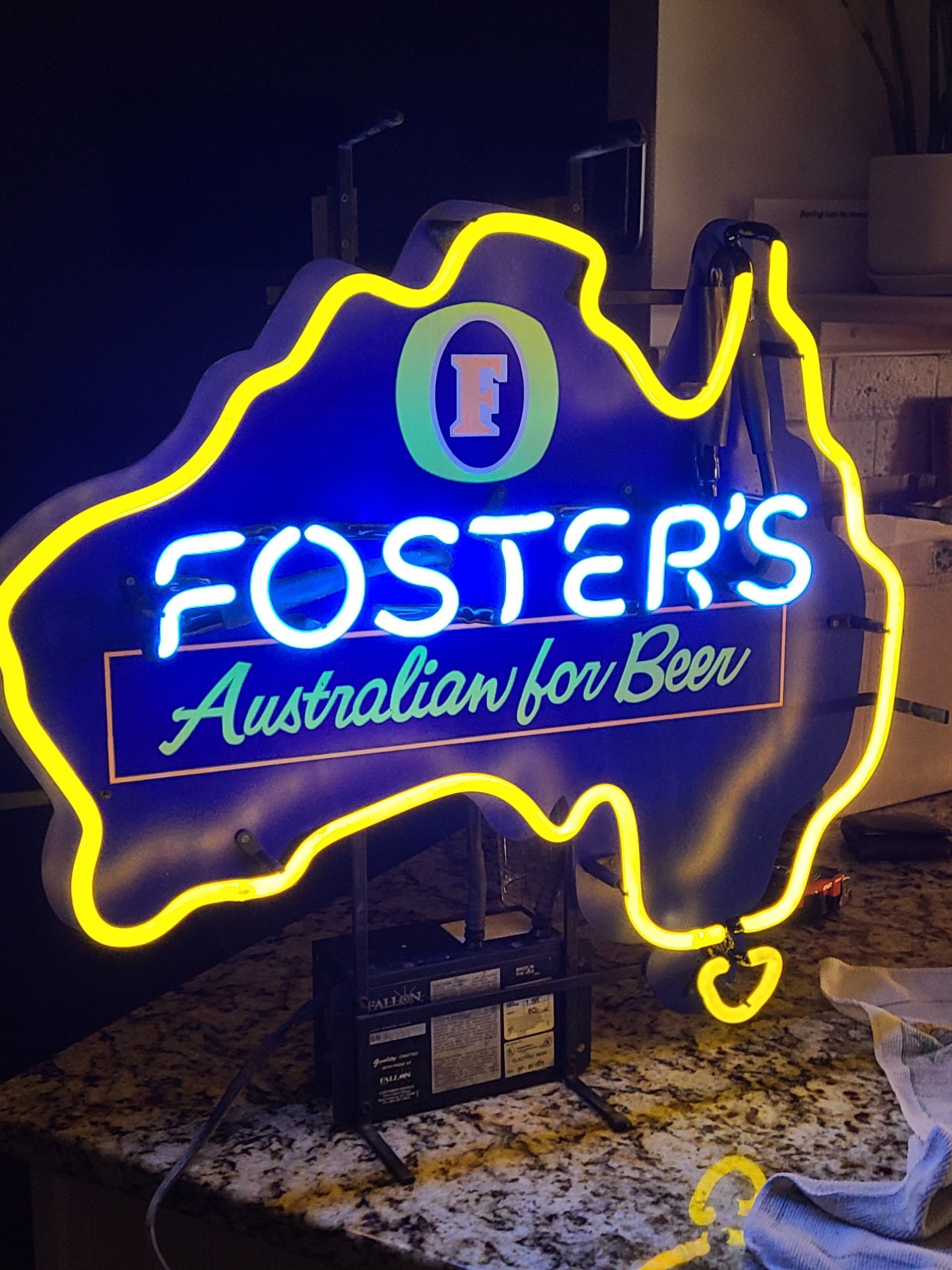 Neon Foster's beer sign shaped like Australia, blue with yellow outline, lit up.