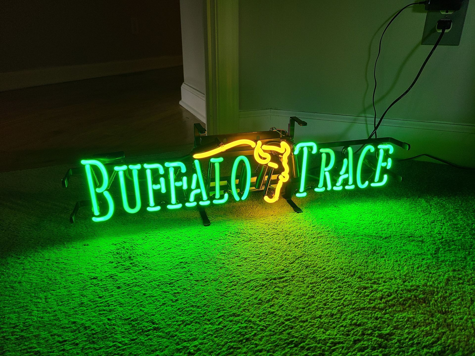 Neon sign for Buffalo Trace whiskey, green and yellow, on green carpet.