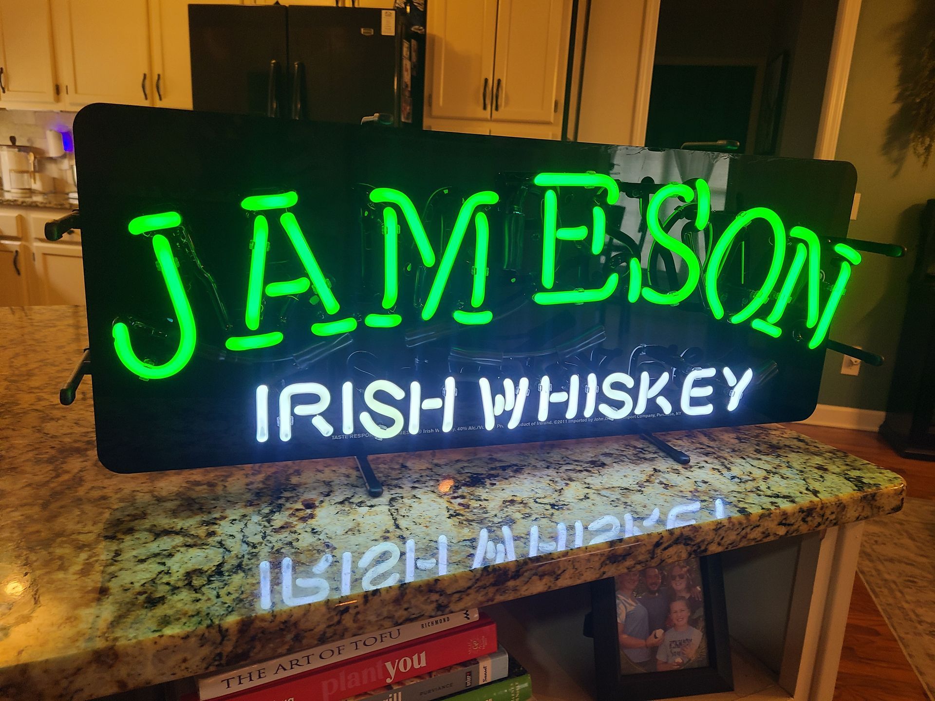 Neon Jameson Irish Whiskey sign, green text on black background, sitting on counter.