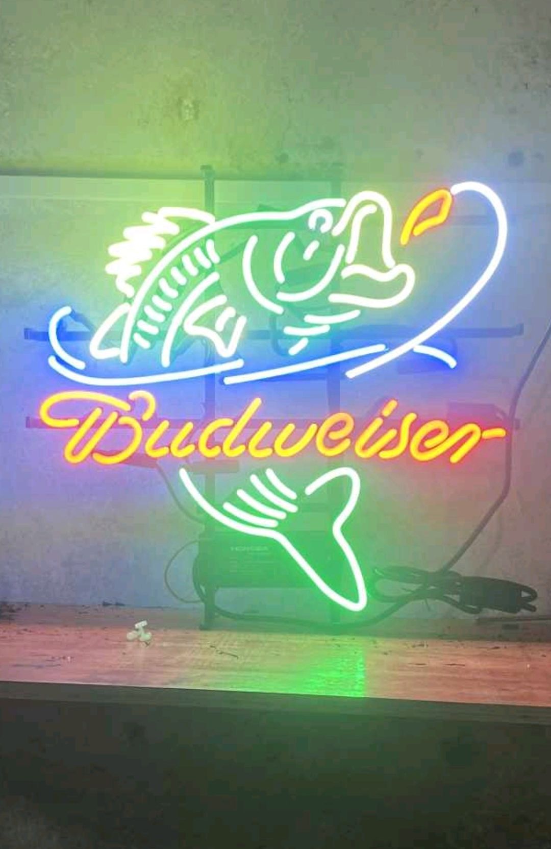 Neon Budweiser sign featuring a fish leaping for a hook, illuminated in green, blue, and orange.
