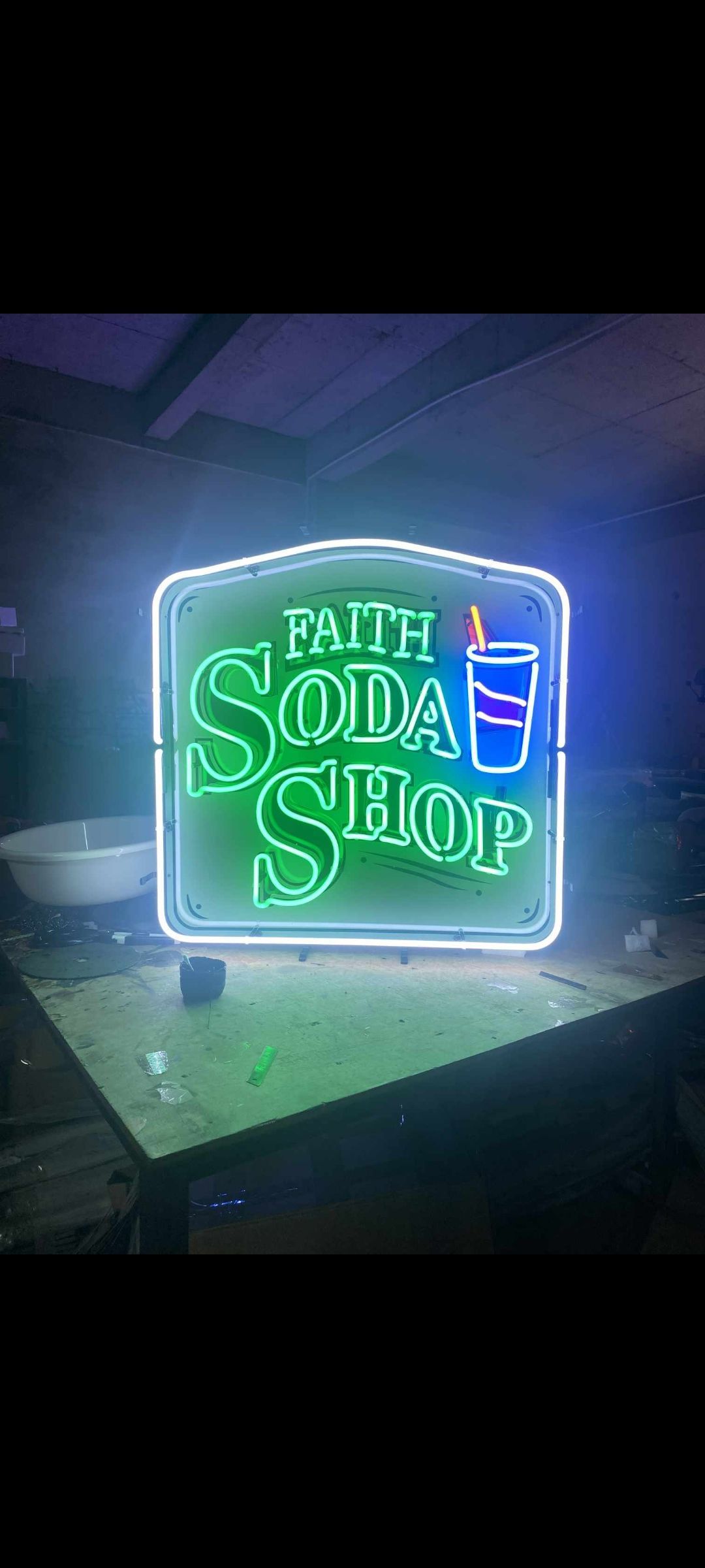 Neon sign for Faith Soda Shop, with green and white lettering, and a blue soda cup illustration.