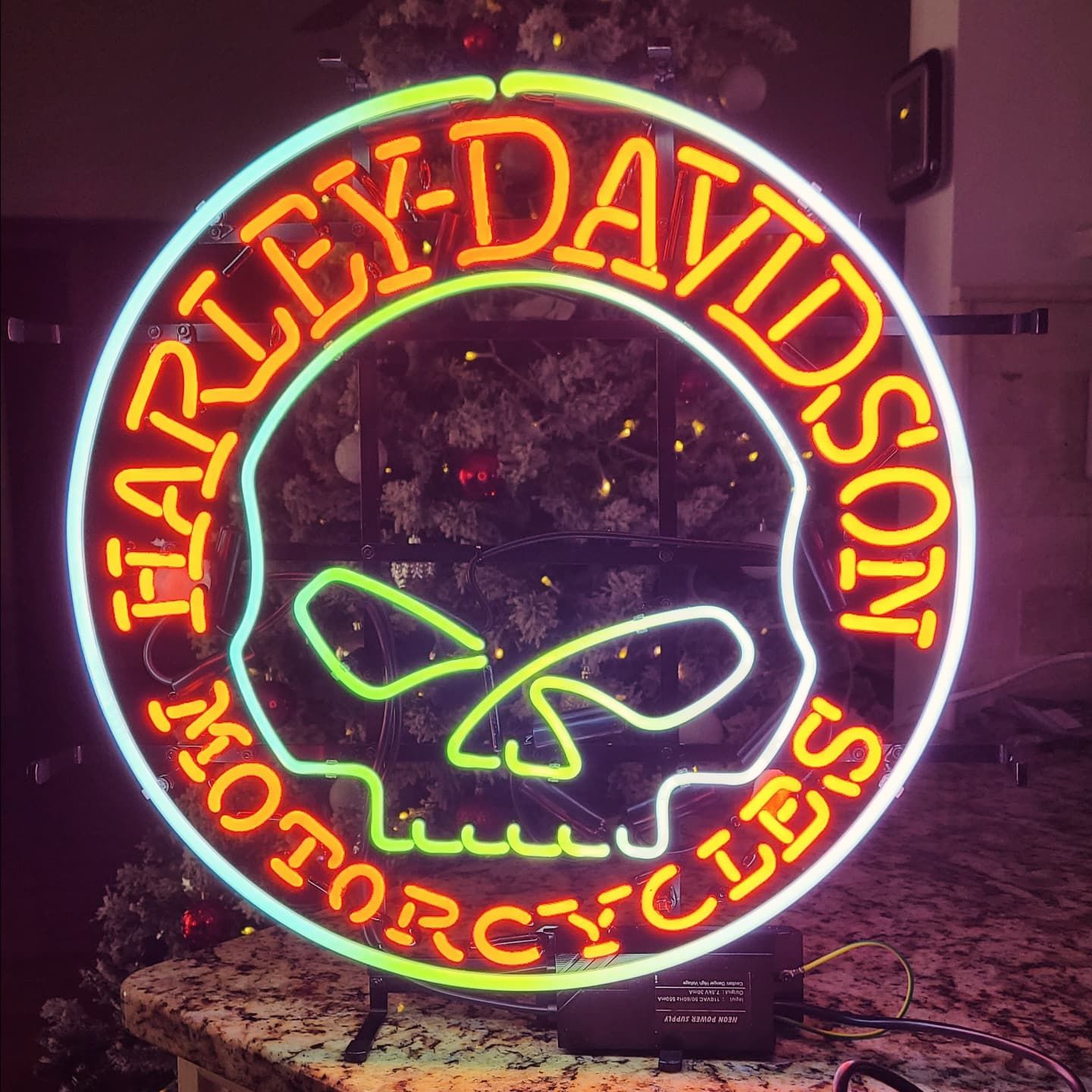 Neon Harley-Davidson sign with orange text and skull on a countertop.