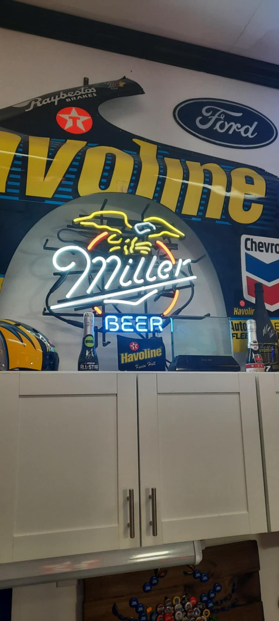 Miller Beer neon sign on a wall above white cabinets. Gasoline and Ford signs are also visible.