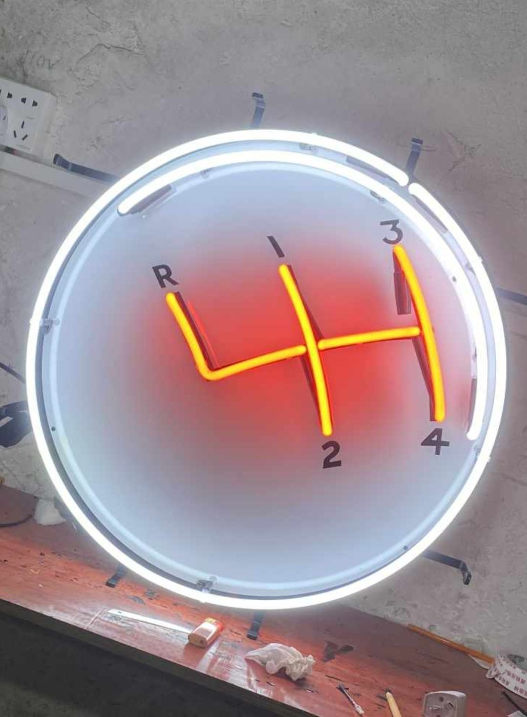 Neon sign of a yellow 4-speed manual transmission gear shift diagram, with a red gradient background inside a circular white border.