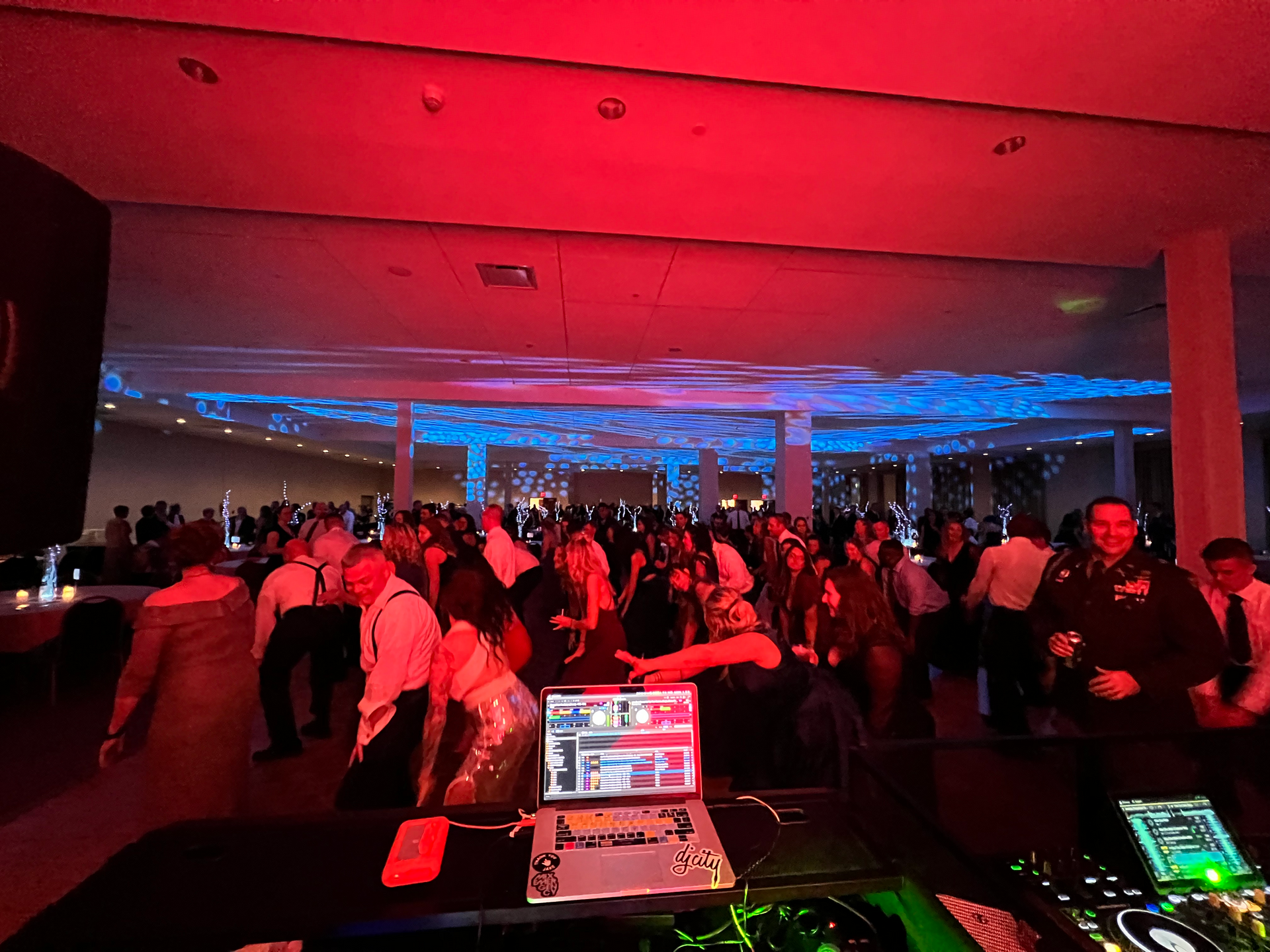 Large party with a DJ setup, dancing crowd, red and blue lighting.