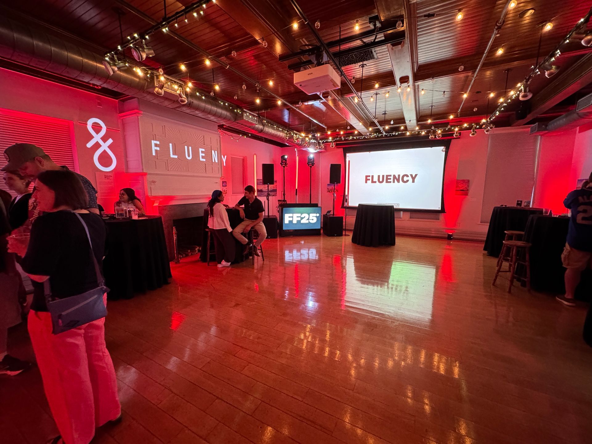 Event space with red lighting, people socializing, screen displaying "FLUENCY."