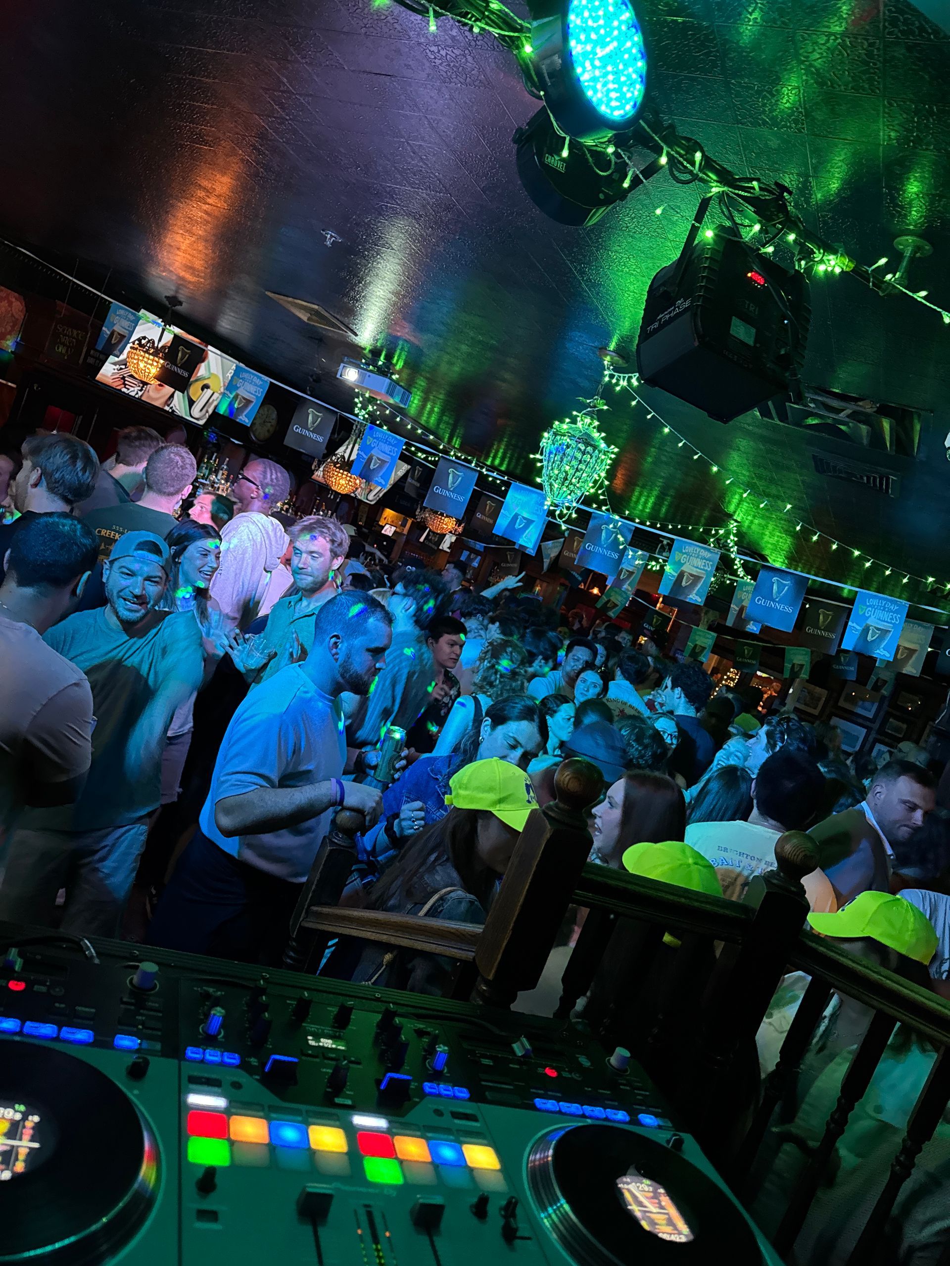 DJ booth overlooking a crowded dance floor with green lighting and people enjoying music.