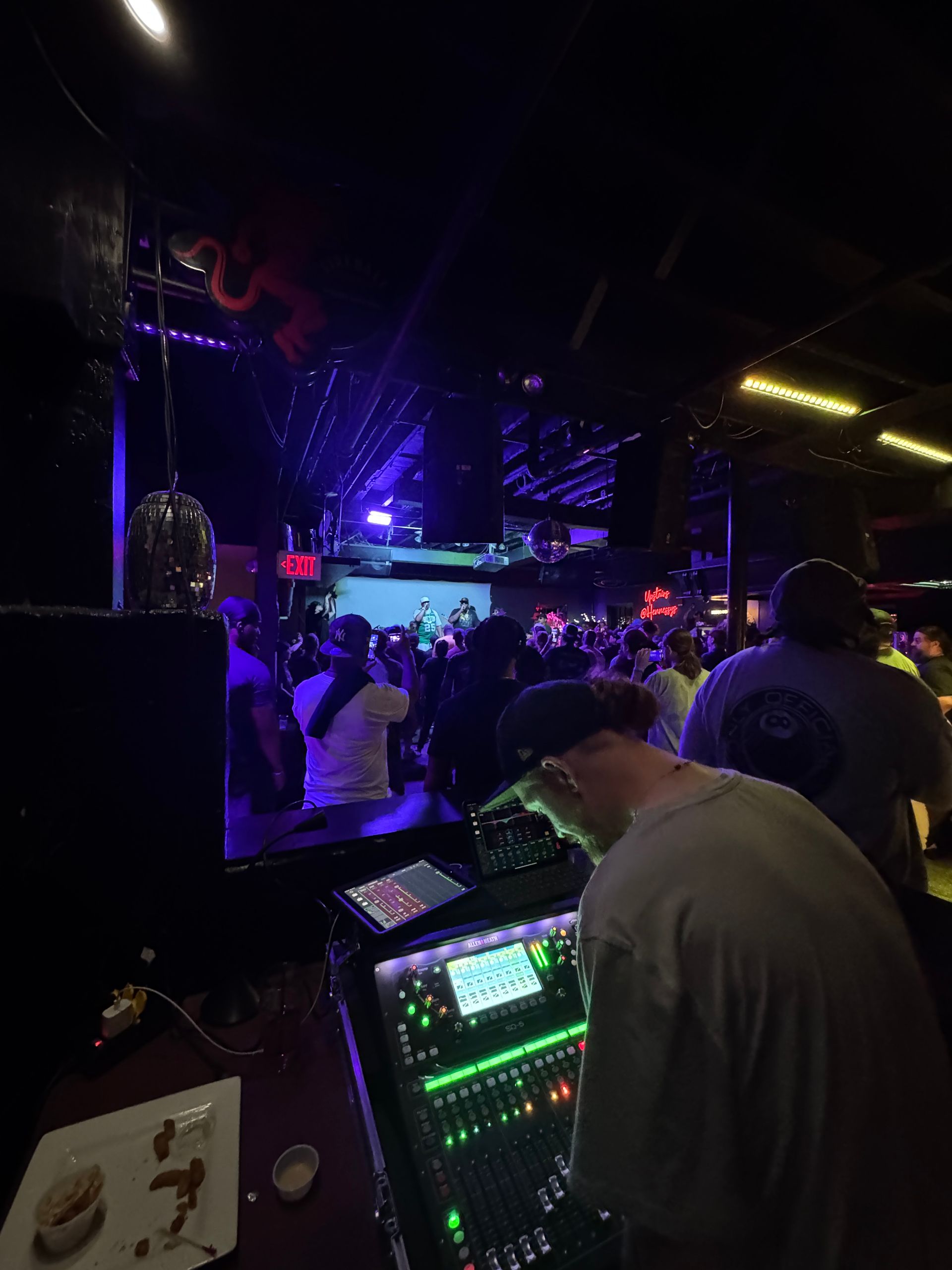 DJ at a crowded nightclub with stage, lights, and people dancing.