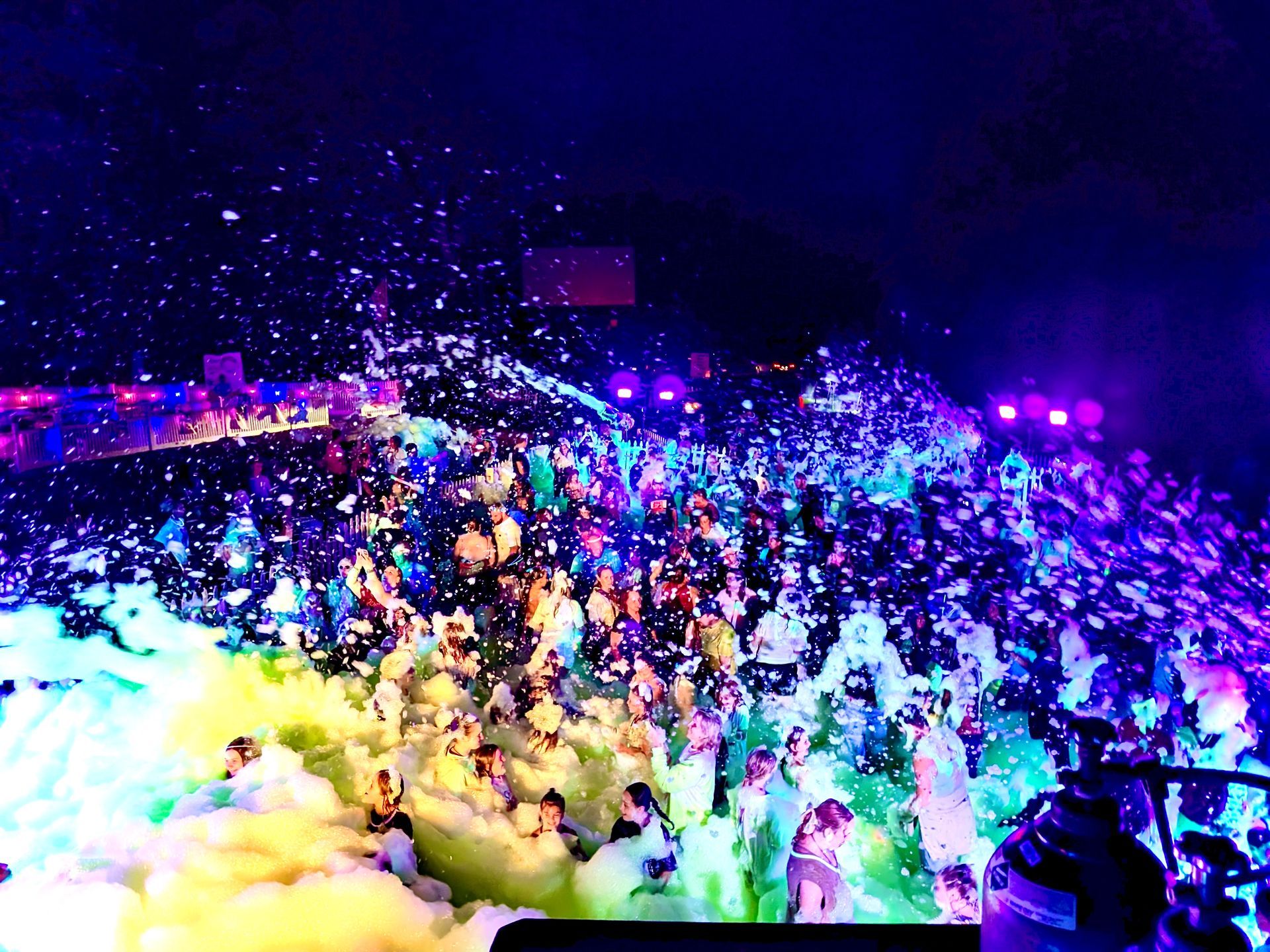 Foam party in a venue. People dancing in colorful foam under purple and blue lights.