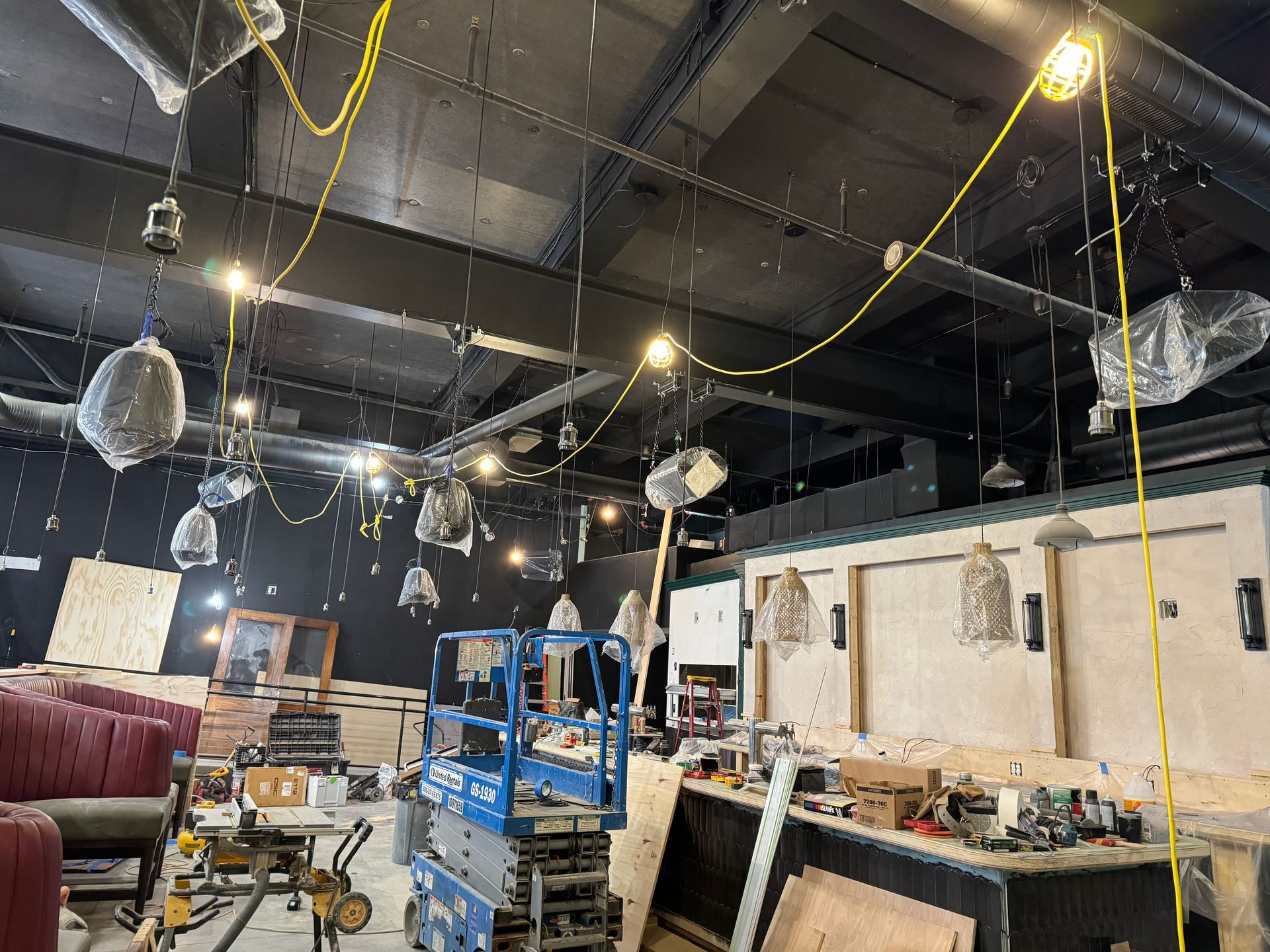 Restaurant under construction: exposed ceiling with lights, tools, lift, bar area, and seating.
