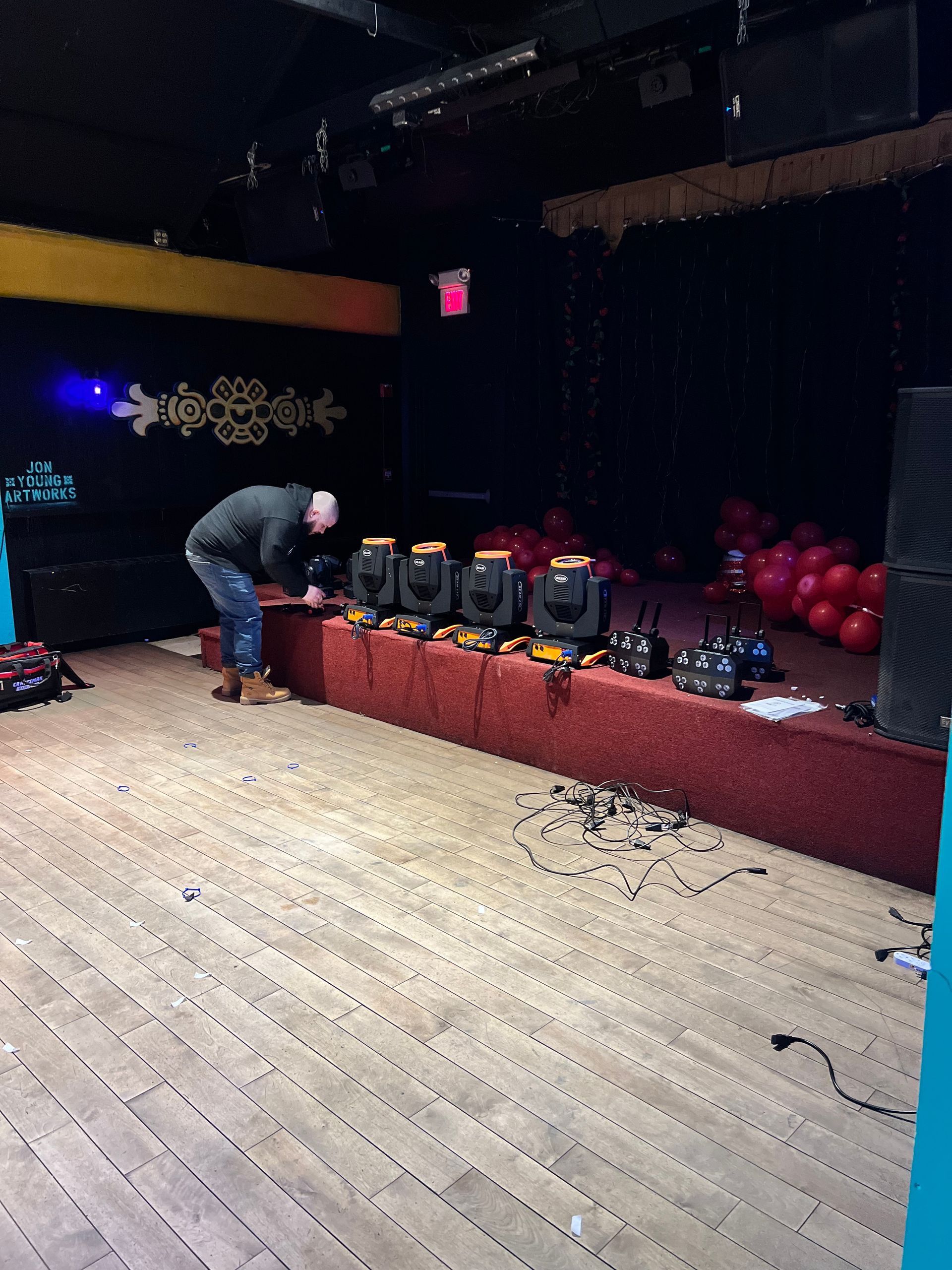Person setting up stage lighting on a stage, with balloons and other equipment.