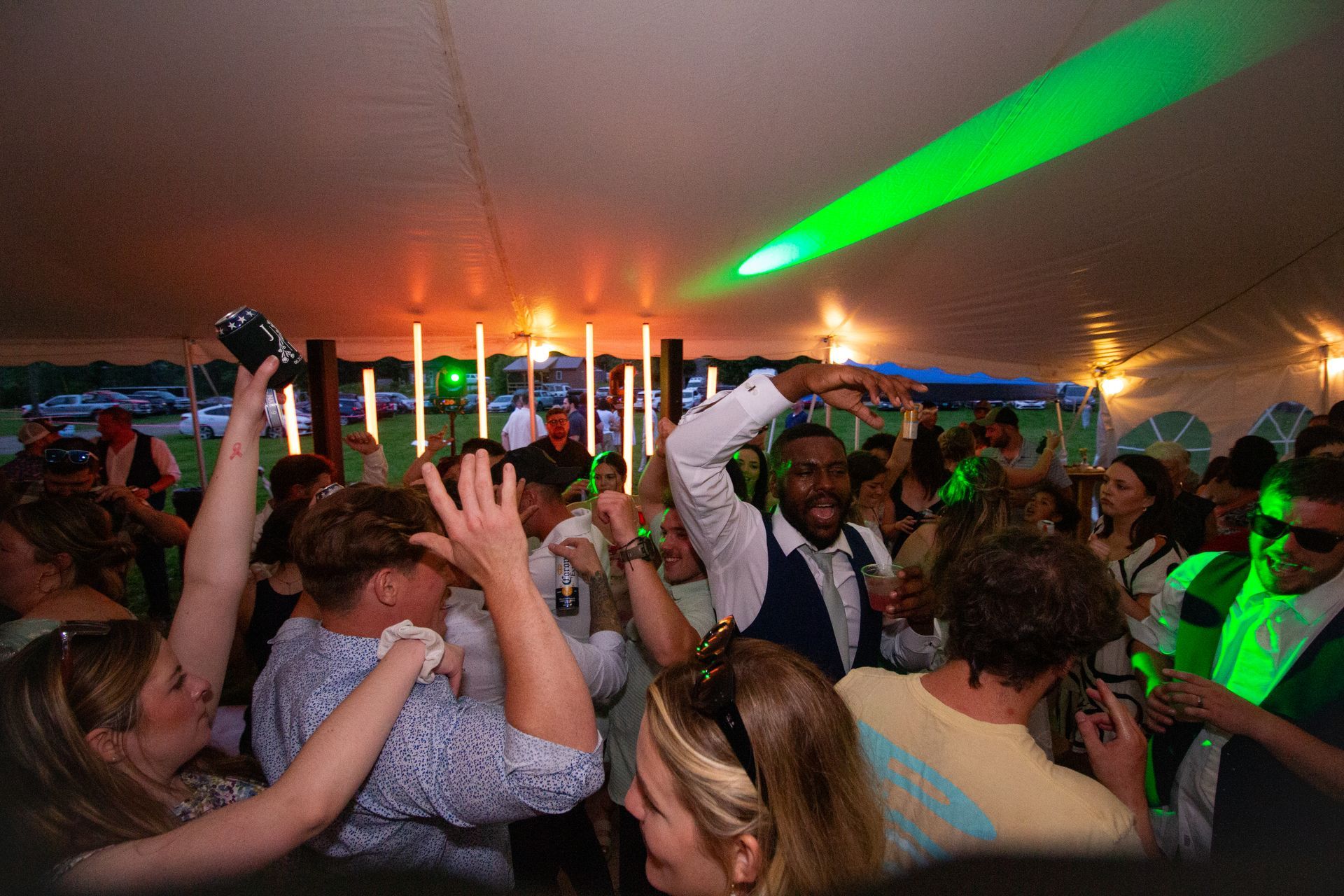 People dancing at a party under a tent. Green laser and orange lights illuminate the crowd.