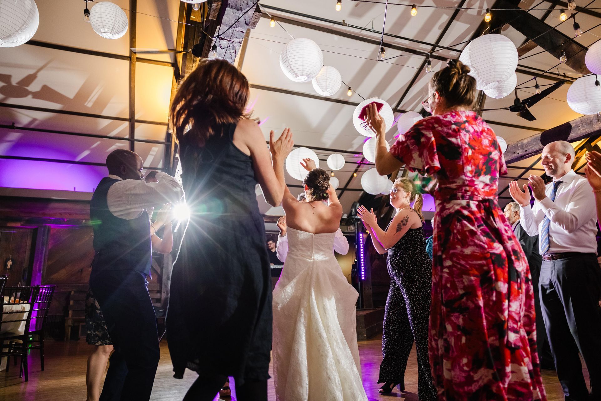 Wedding reception: Bride dancing, surrounded by guests. White paper lanterns hang overhead.