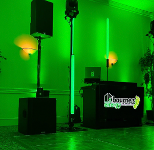 Green lit DJ setup with speakers and light columns.