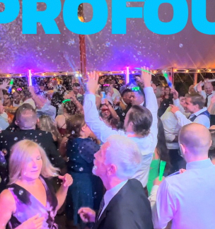 People dancing at a party with glow sticks under colorful lights.