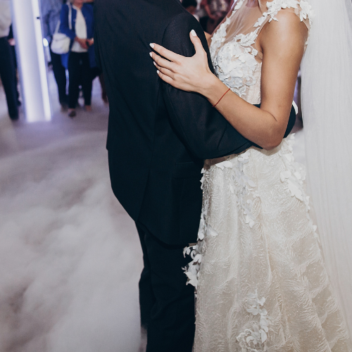 Bride and groom dancing at wedding. Bride in white lace gown, groom in black suit. Smoke on floor.