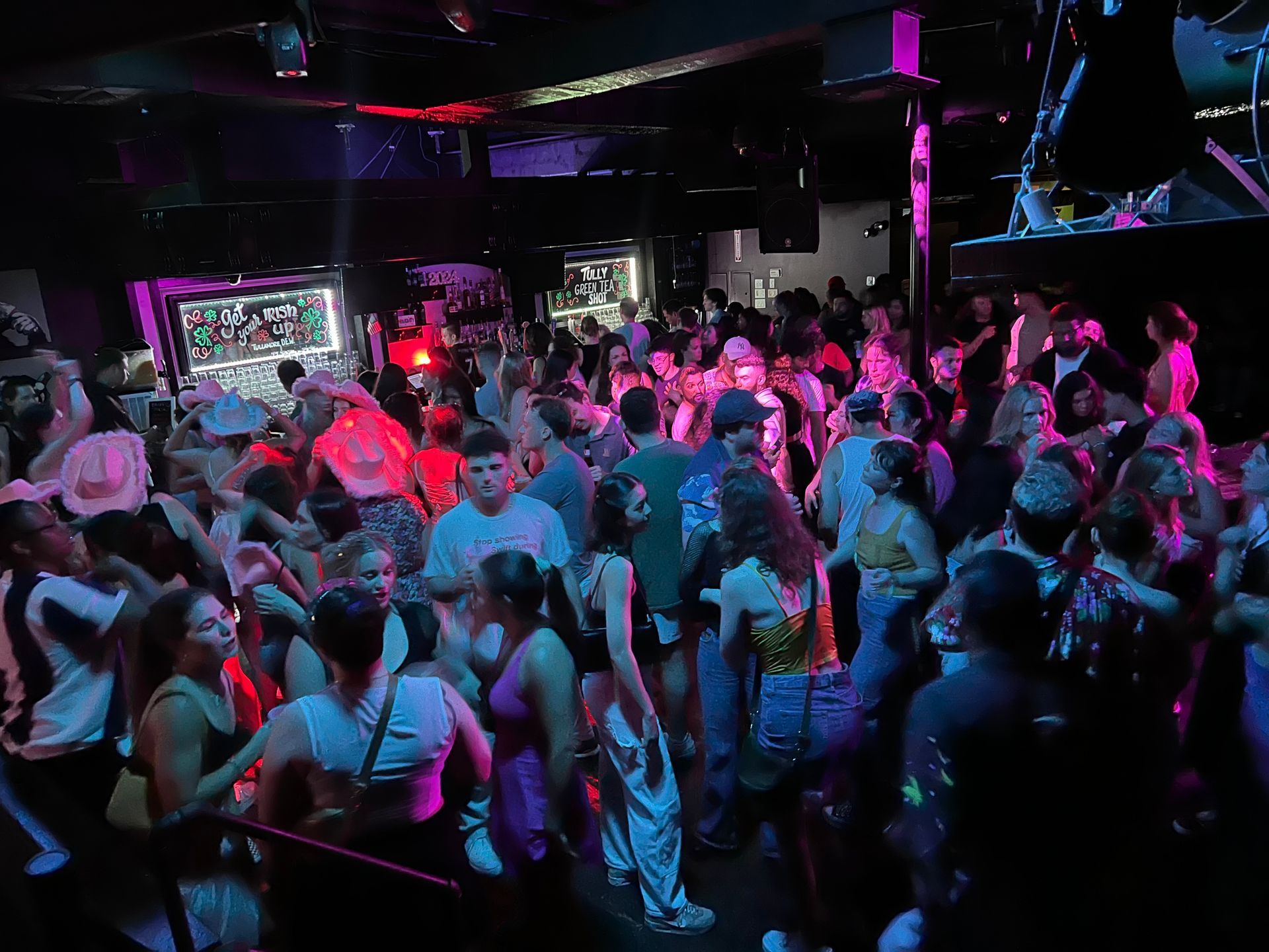 People dance in a crowded, dimly lit club with colorful lights.