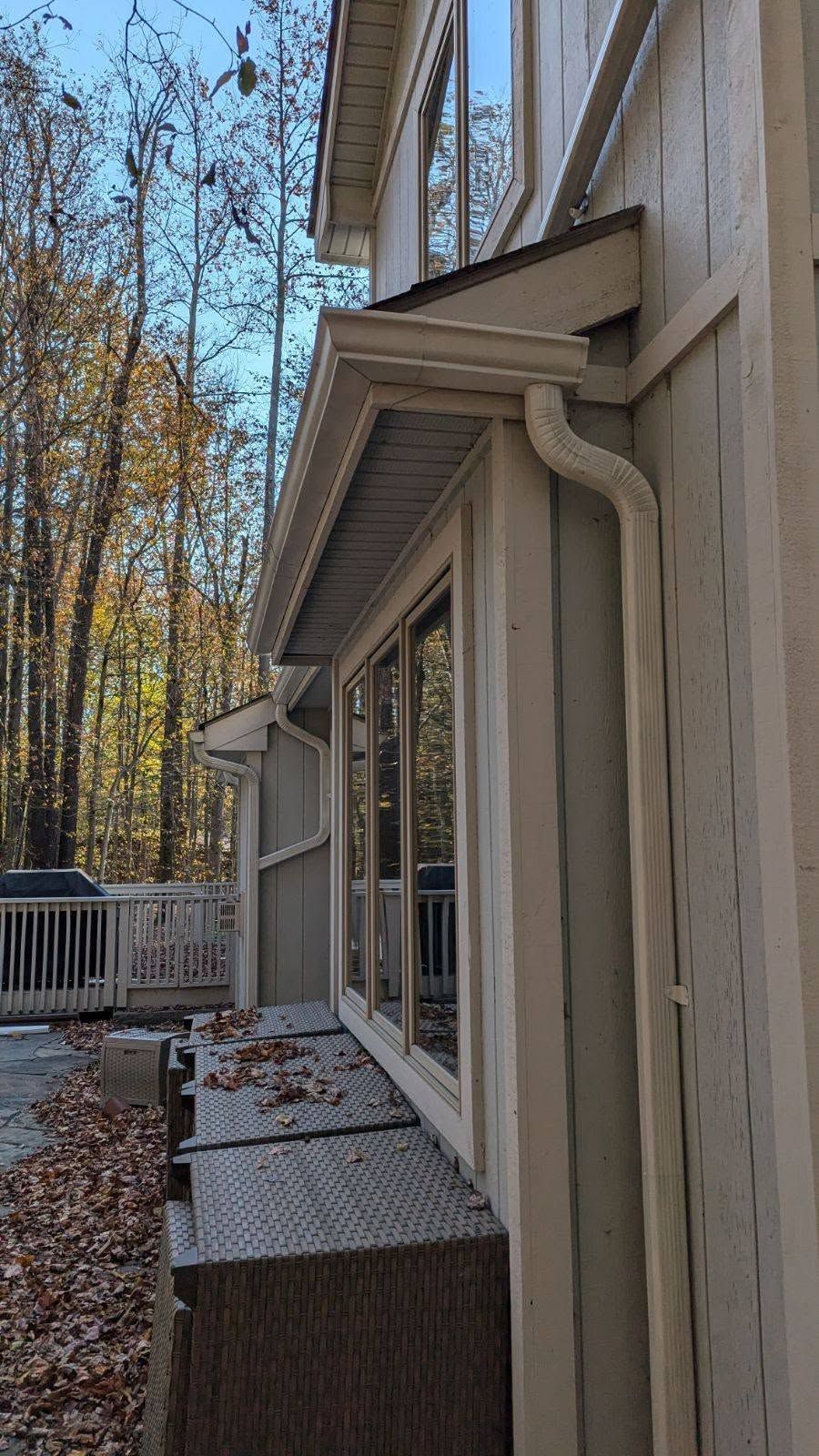 Side view of a beige house with windows, deck railings, and autumn trees nearby