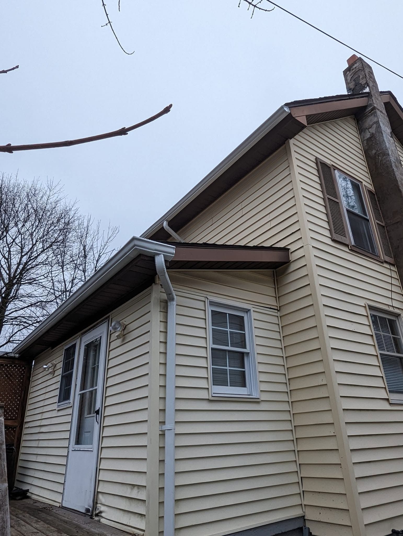 Small beige house with white trim, a white door, and a tree branch overhead on an overcast day