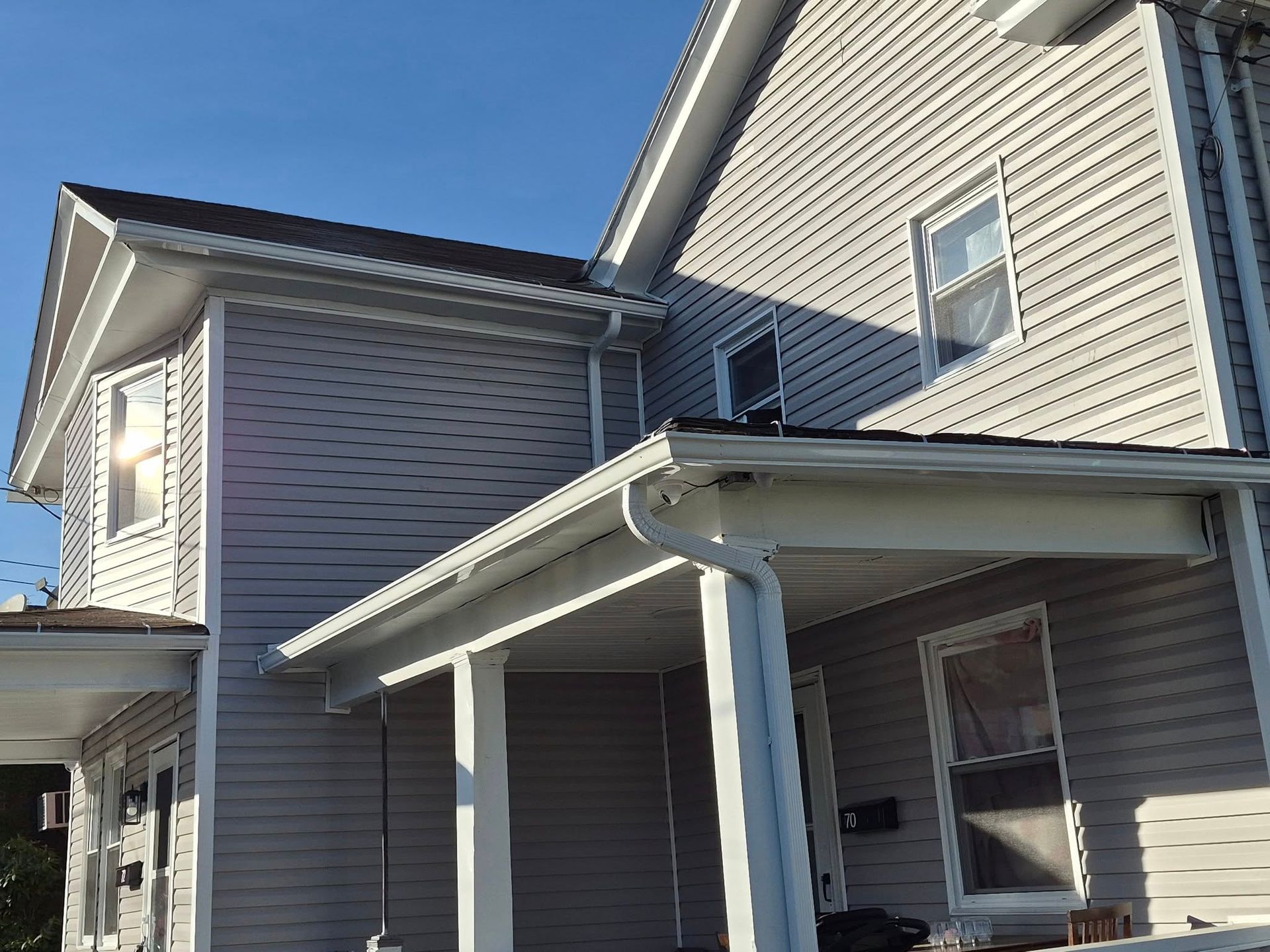 Two-story beige house exterior with white trim, covered porch, and blue sky