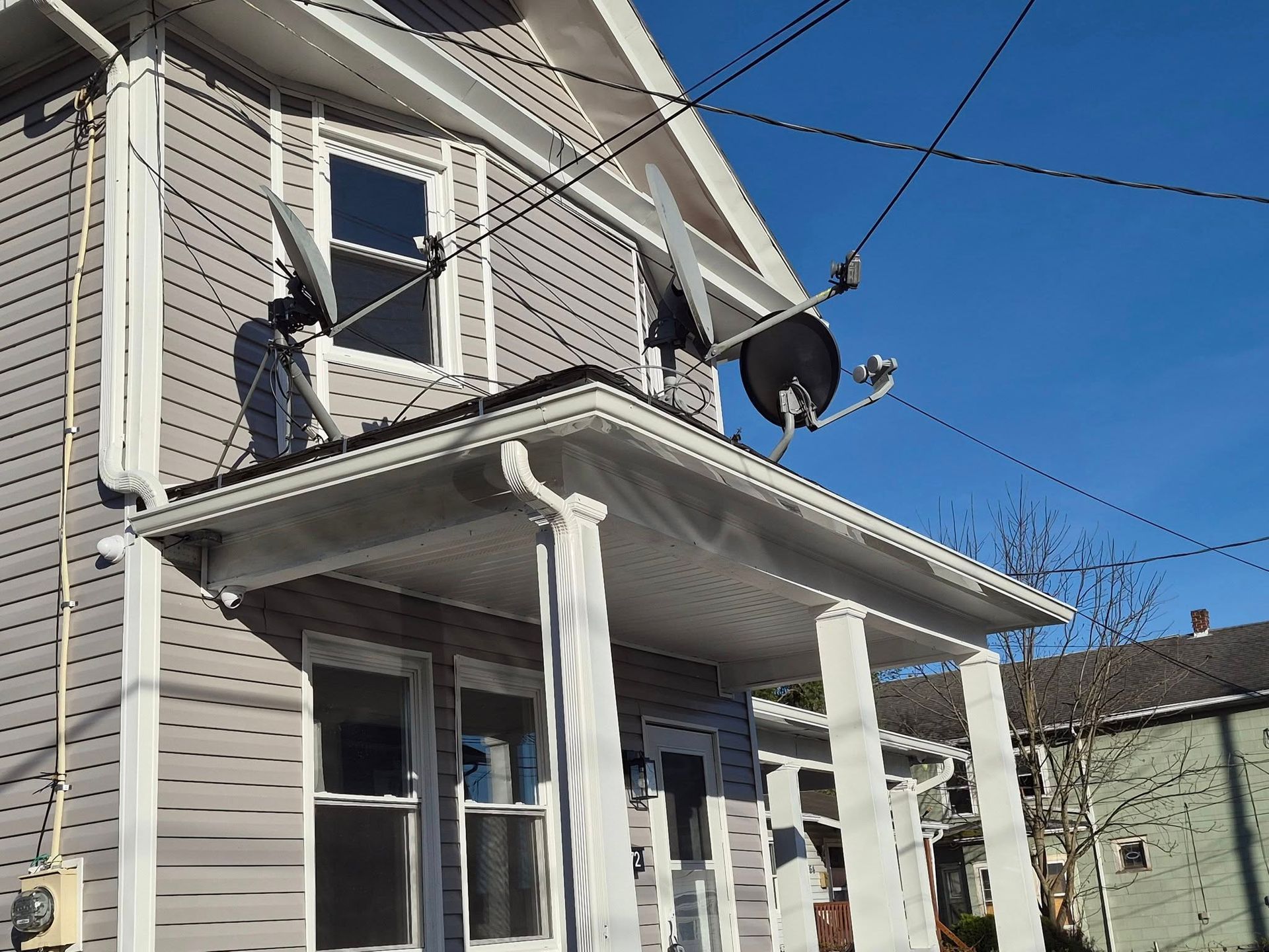 Two-story gray house with white porch columns and a satellite dish against a blue sky