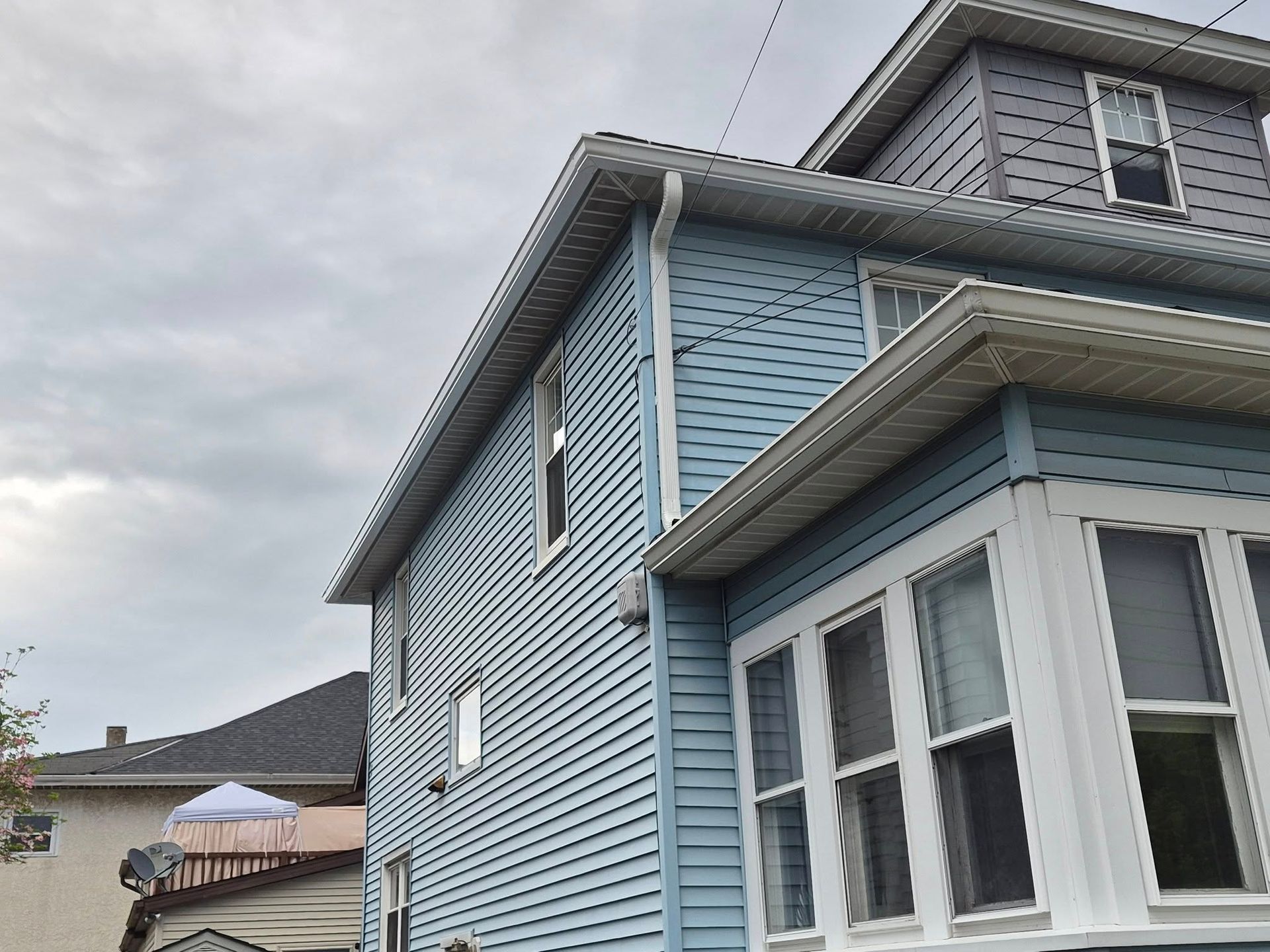Blue two-story house with white trim and bay windows under a cloudy sky