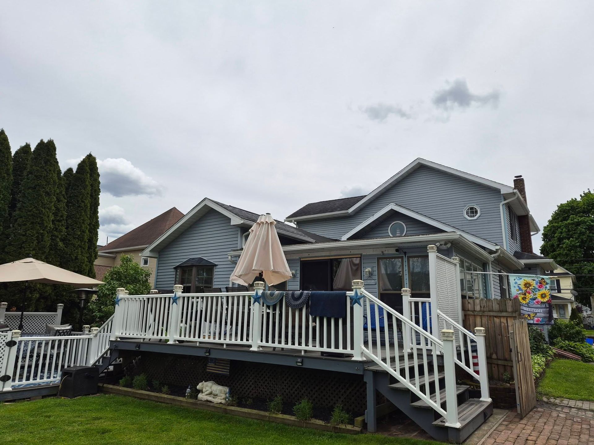 Gray house with a white deck, stairs, and patio umbrellas on a cloudy day