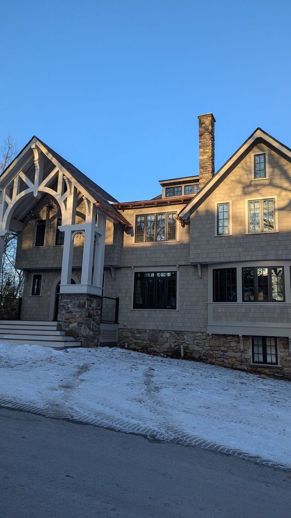 Snow-covered stone house with gabled roof and large windows on a sunny winter day