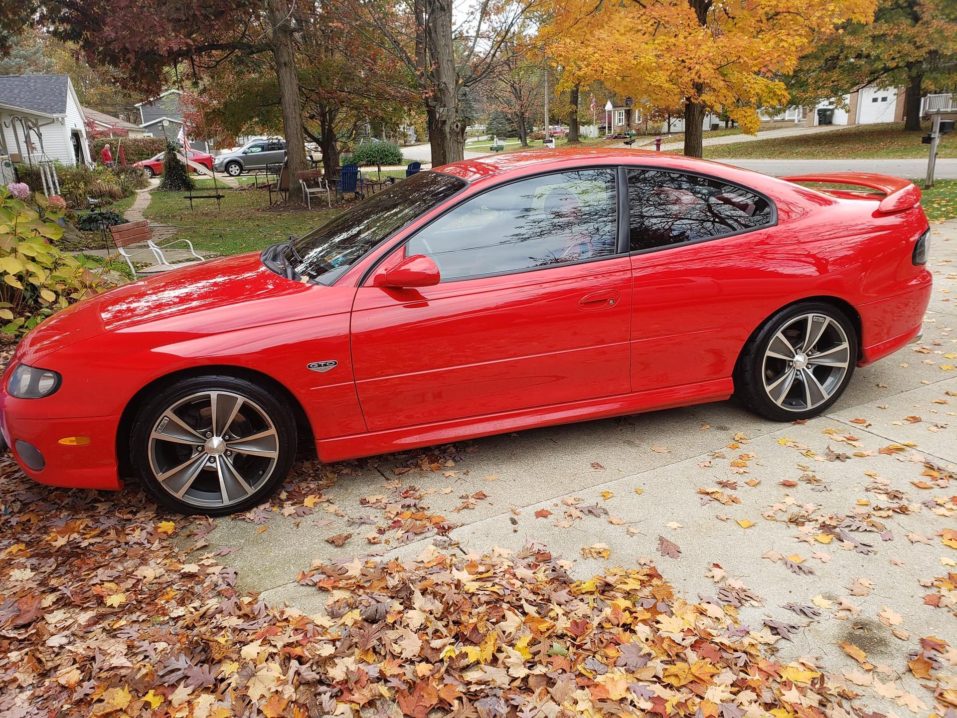 A red sports car is parked in a driveway covered in leaves.