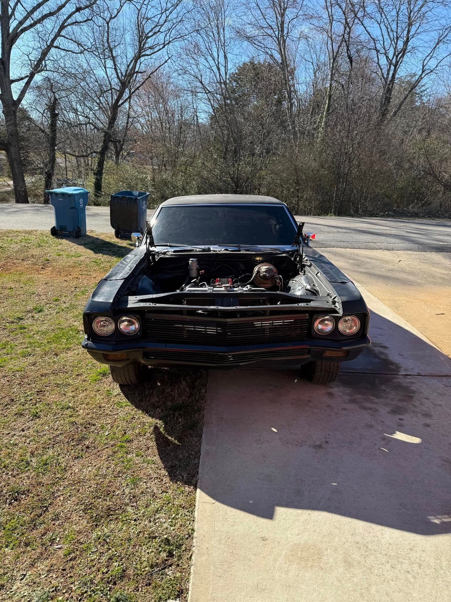 A black car with the hood up is parked in a driveway.