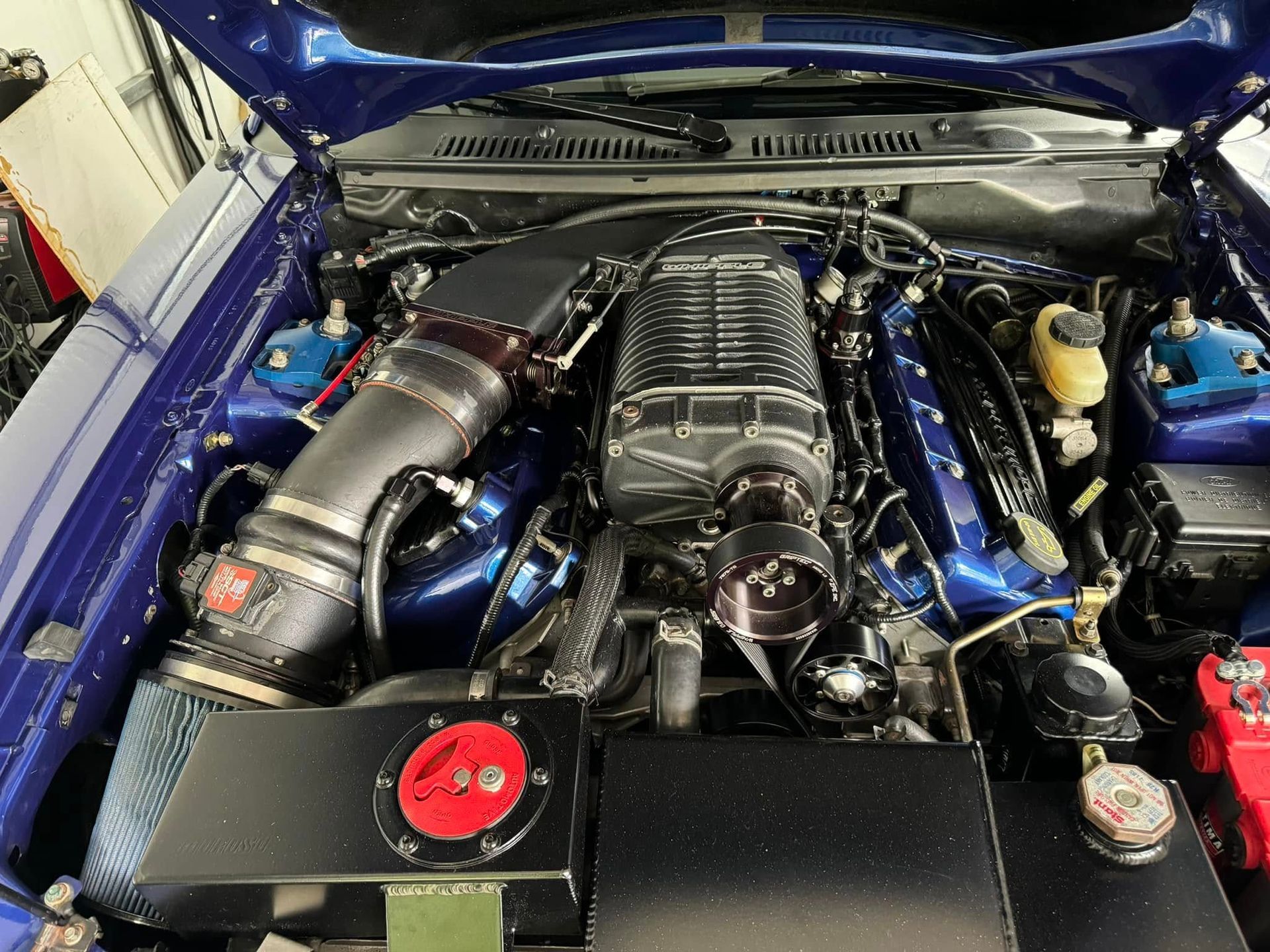 The engine of a blue car is shown with the hood open.