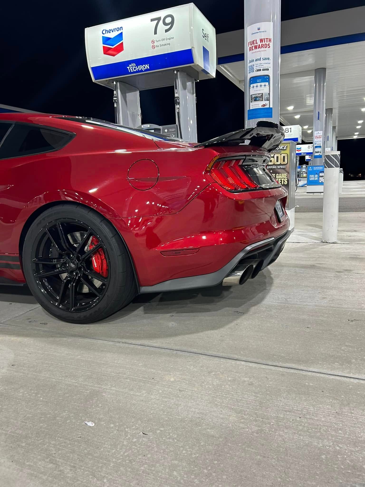 A red mustang is parked at a gas station.