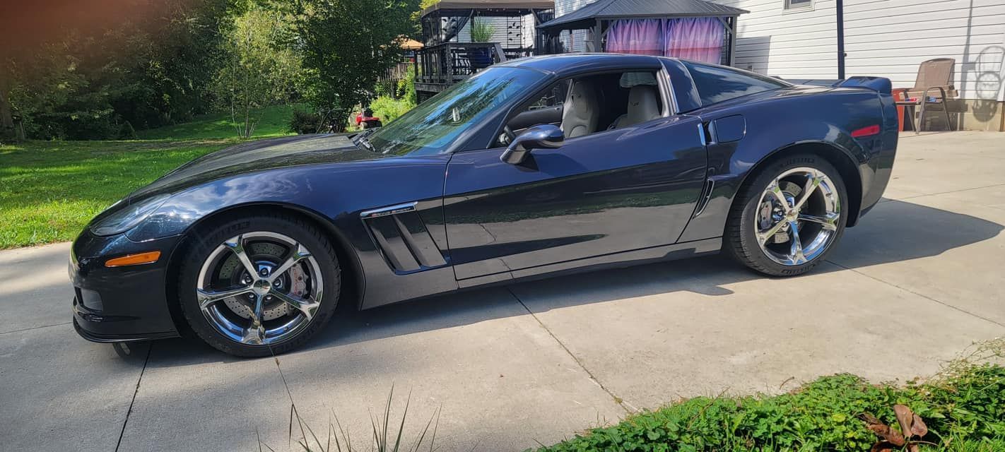 A blue corvette is parked on the side of the road in a driveway.