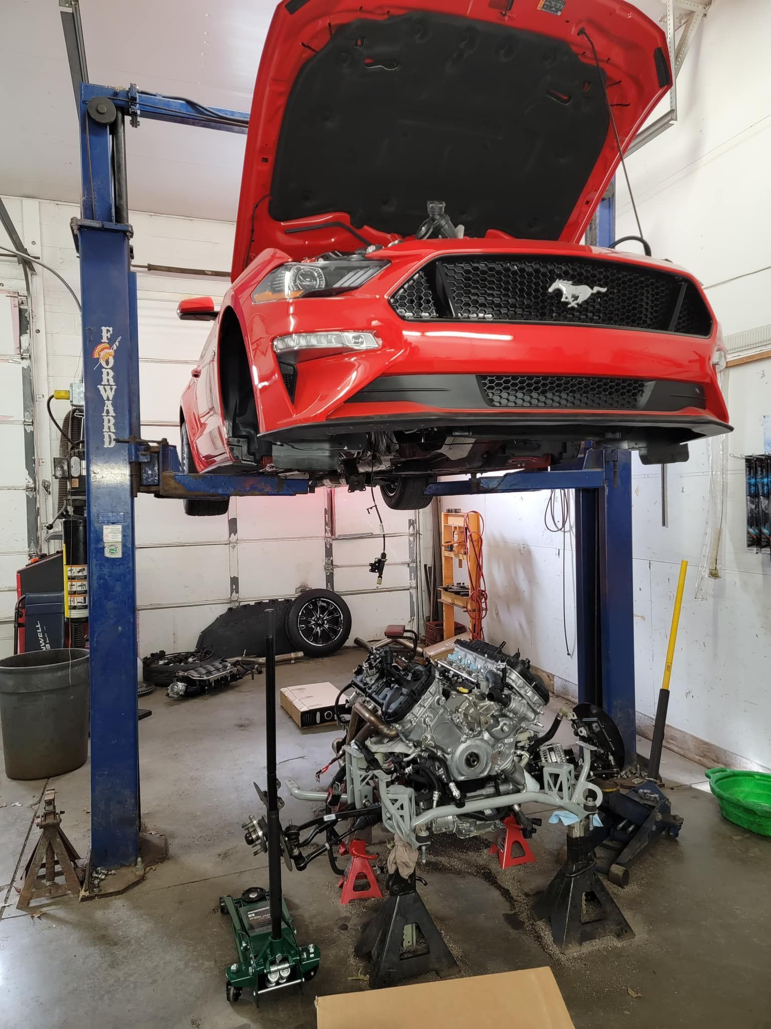 A red mustang is on a lift in a garage with the hood up.