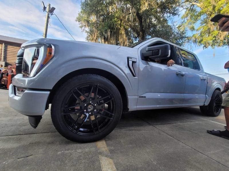 A silver truck with black wheels is parked in a parking lot.