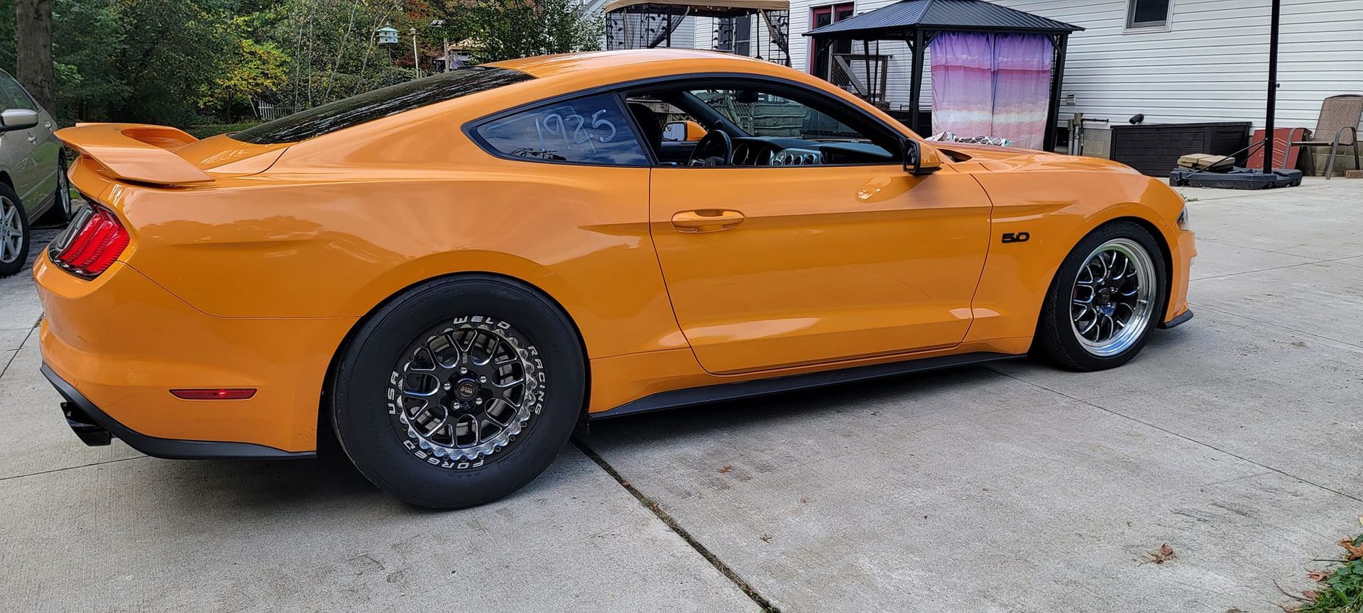 A yellow mustang is parked in a driveway next to a house.