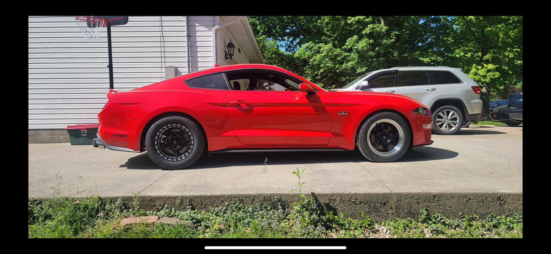 A red mustang is parked in a driveway next to a house.