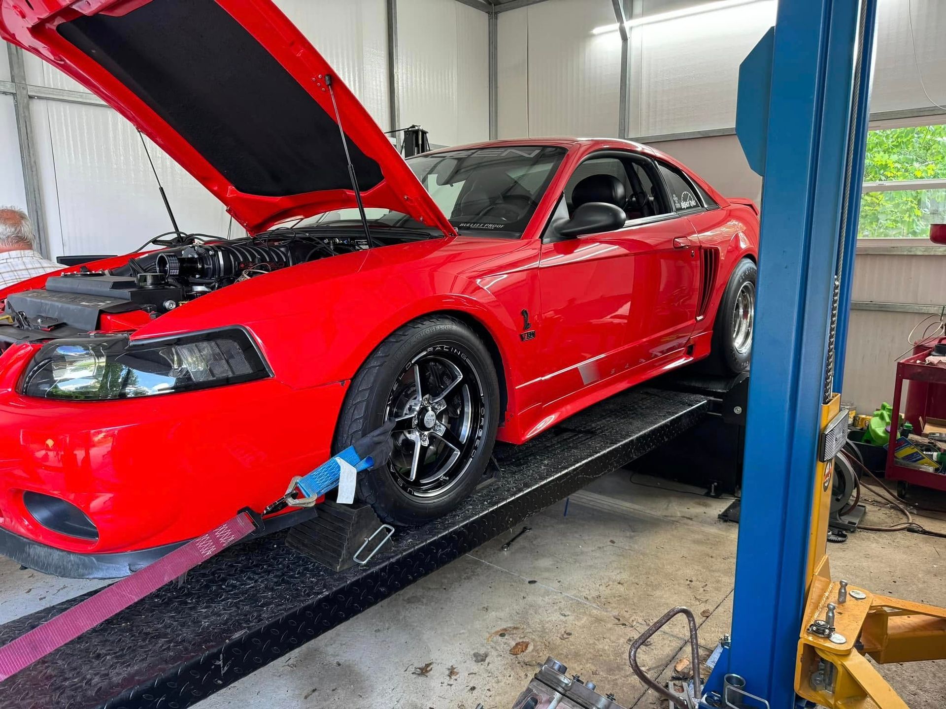 A red mustang is sitting on a lift in a garage.