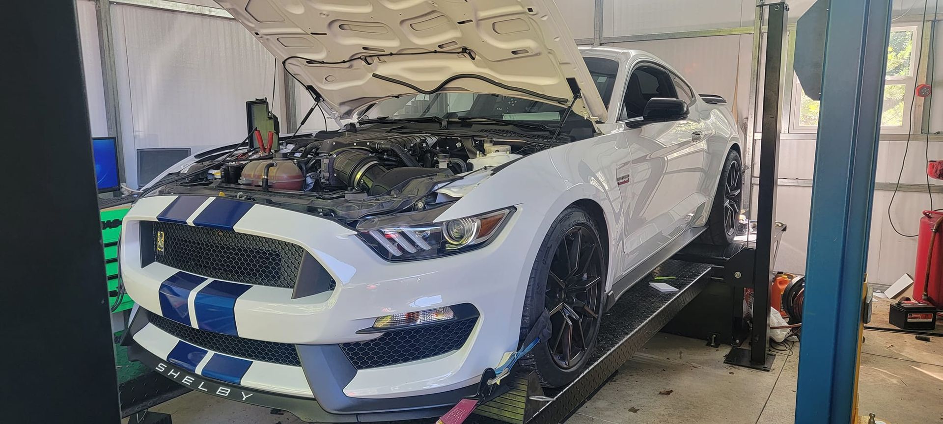 A white ford mustang is sitting on a lift in a garage.