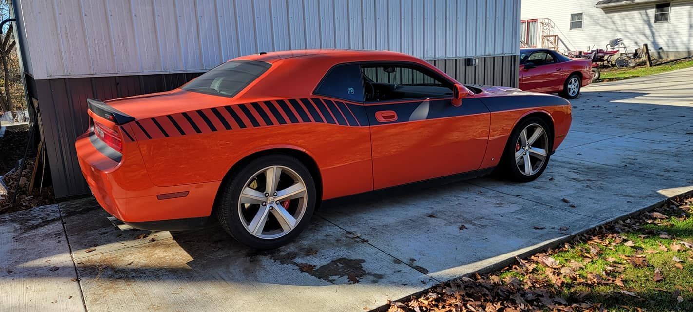 A red dodge challenger is parked in a driveway next to a house.